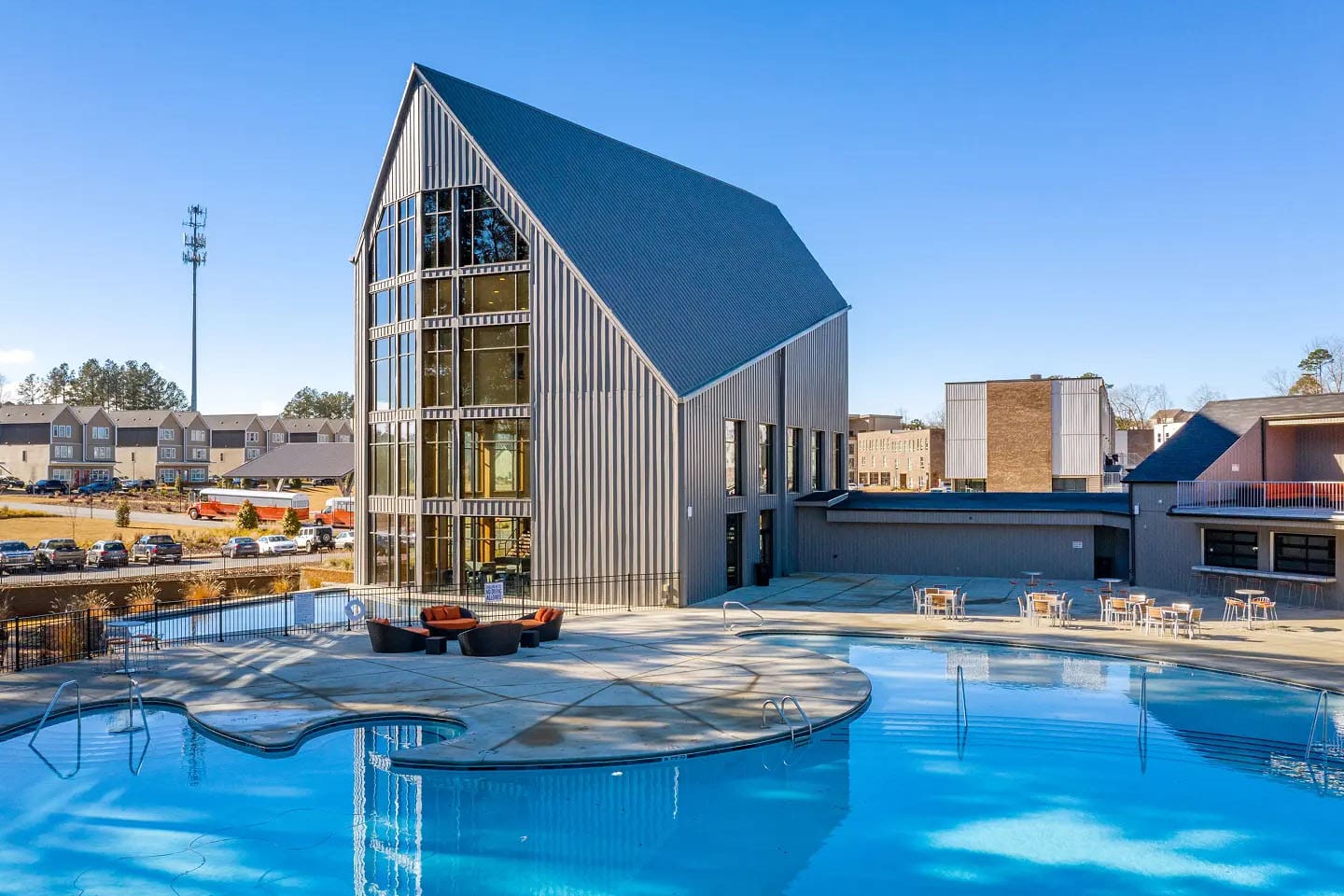 Large pool with seating and behind is a large building with open windows.