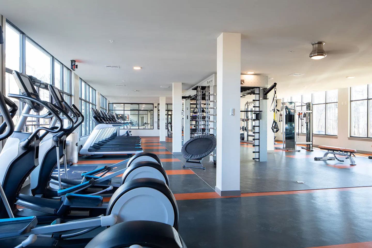 Fitness center with various cardio equipments and large open windows.